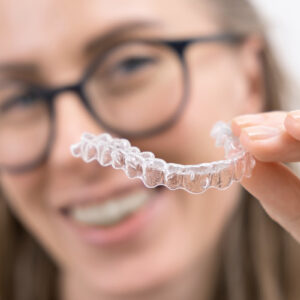 smiling woman using clear plastic removable braces aligner or whitening tray. dental orthodontic care.